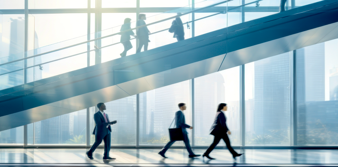 5 People walking through an office building. Stairs to the upper levels in the background.
