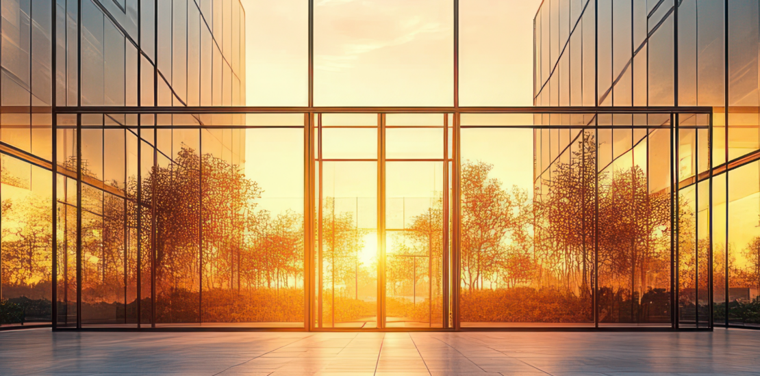 Sunlit modern glass building atrium with reflective facades, empty tiled floor, and warm golden hour glow conveying calm and serenity