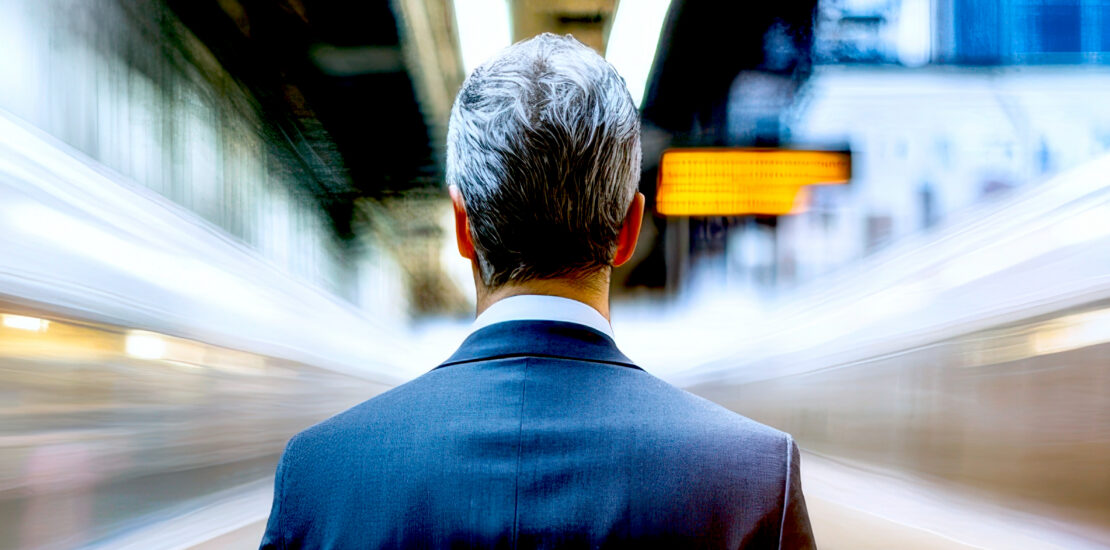 A man in a suite standing between two moving, blurry trains.